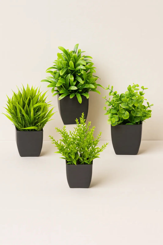 Four artificial green plants in black pots on a white background