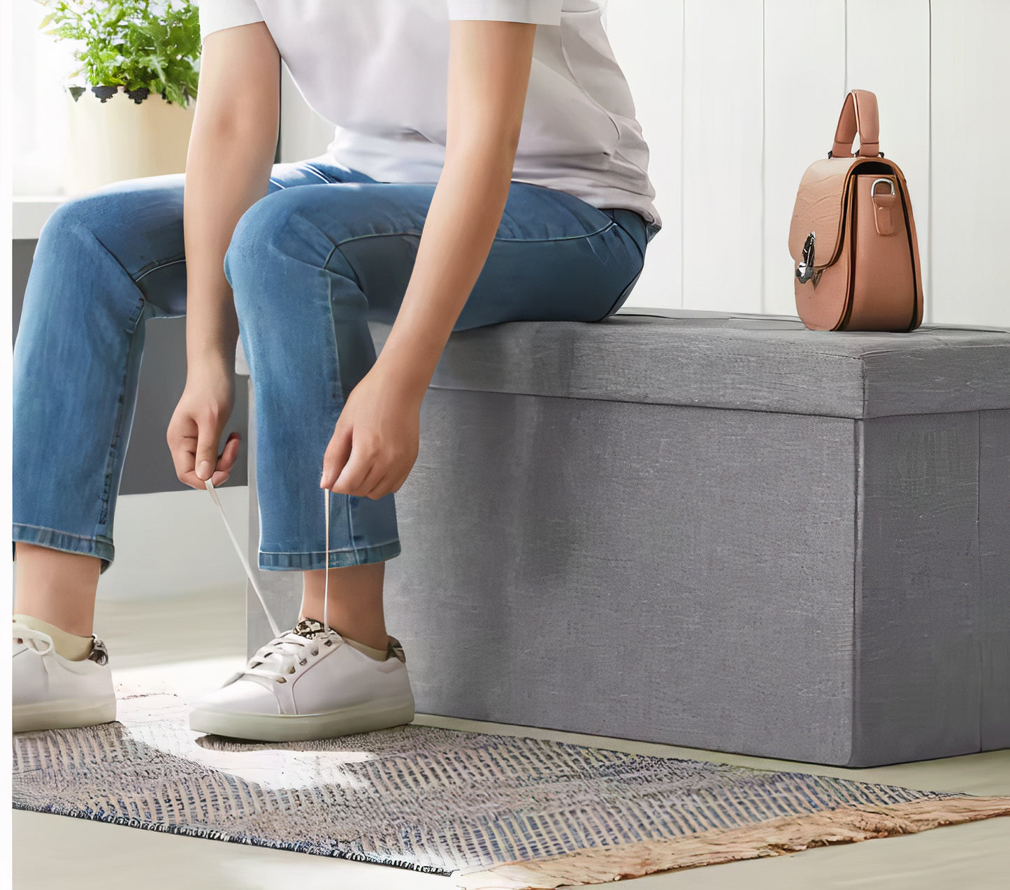 Person sitting on a gray storage bench tying shoelaces in a home setting.