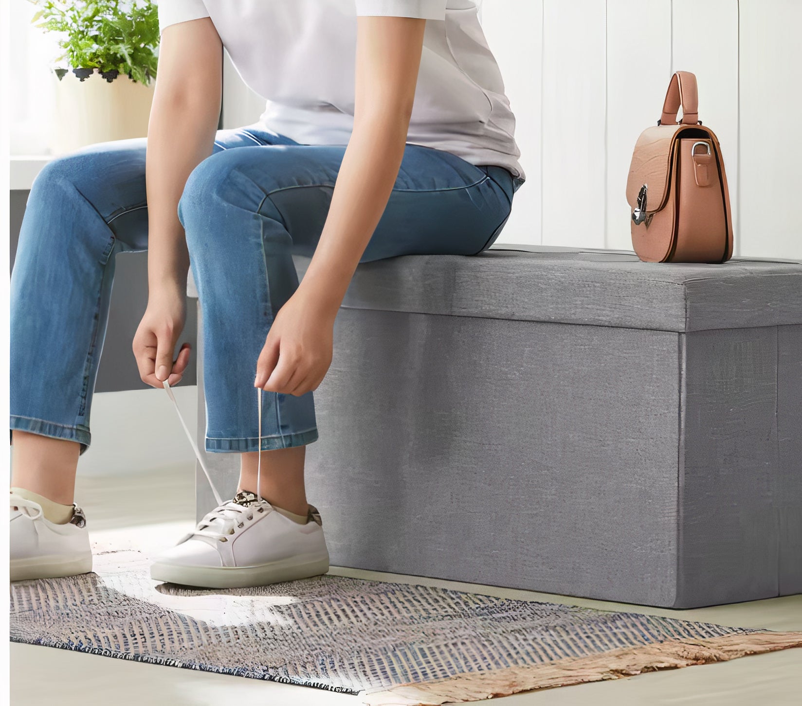 Person sitting on a gray storage bench tying shoelaces in a home setting.