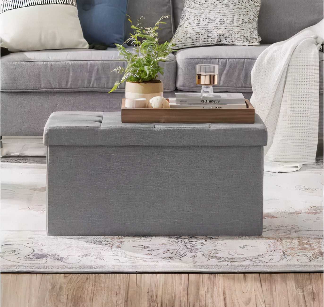 Gray storage ottoman in a living room setting with a plant and decorative items on top.