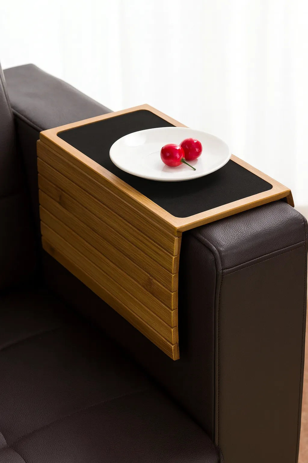 Bamboo armrest table attached to a sofa with a plate of cherries on a white background
