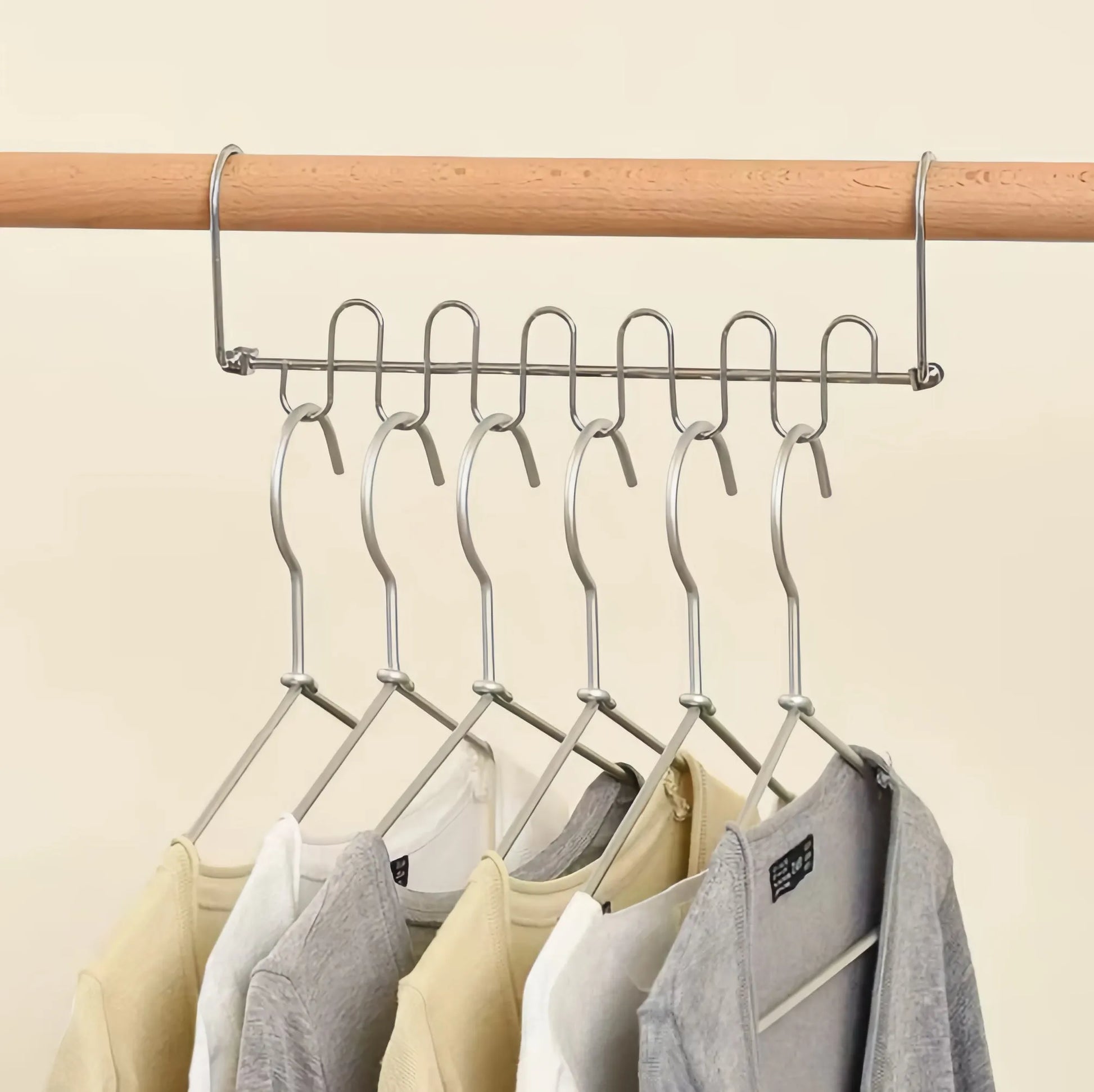 Metal hangers with clothes on a wooden rod against a beige background