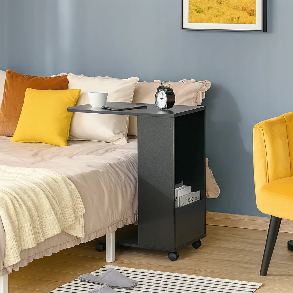 Black side table with a cup, tablet, and alarm clock next to a bed with colorful pillows and a yellow chair.